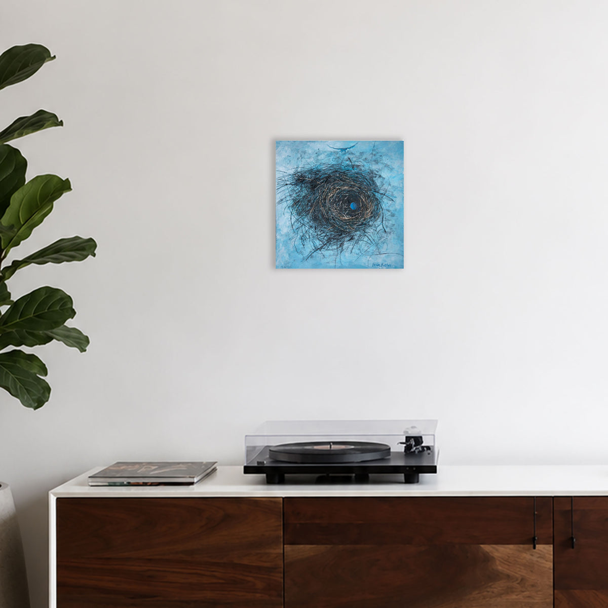 A square abstract canvas print featuring a textured blue and black nest, displayed on a white wall above a wooden credenza.