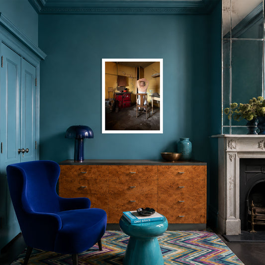 A framed art print featuring a portrait of a woman in a vintage kitchen, displayed on a dark teal wall in a contemporary styled living room.