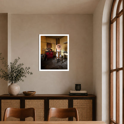 A framed art print depicting a vintage scene of a woman in a wooden chair with a red range, displayed on a beige wall in a modern dining room setting.