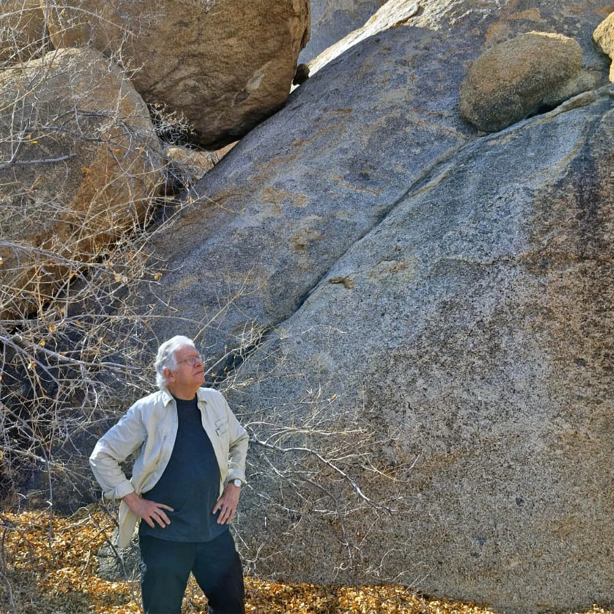 Painter Hein Botha in Namibia standing beside a large rock, hands on hips, contemplating his surroundings. 