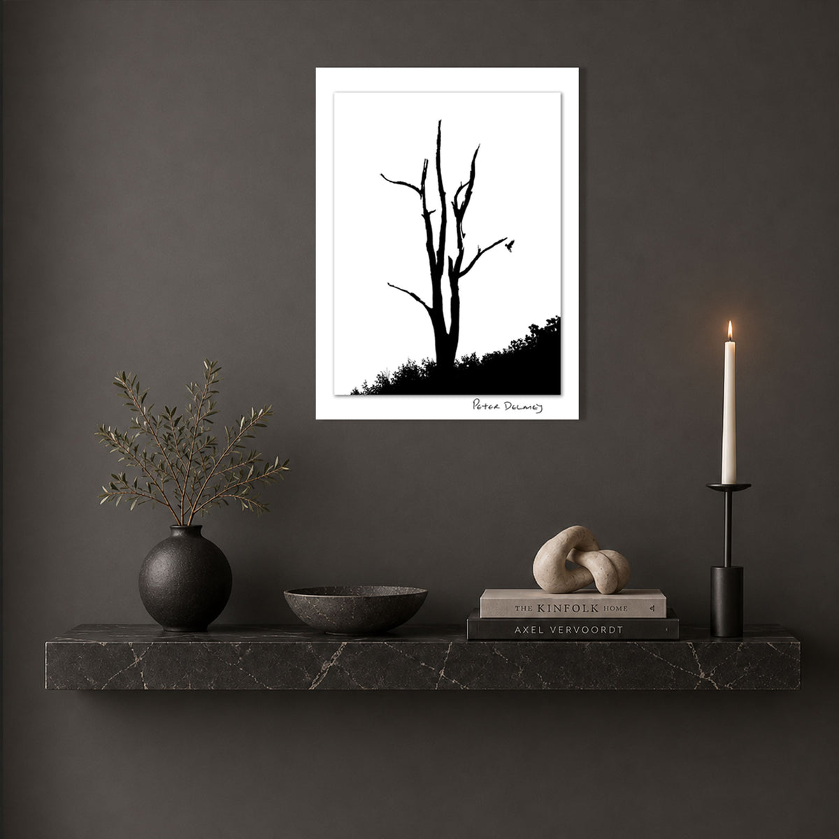 Peter Delaney’s black-and-white photograph of a leafless tree, framed in white and displayed above a dark marble shelf in a contemporary interior.