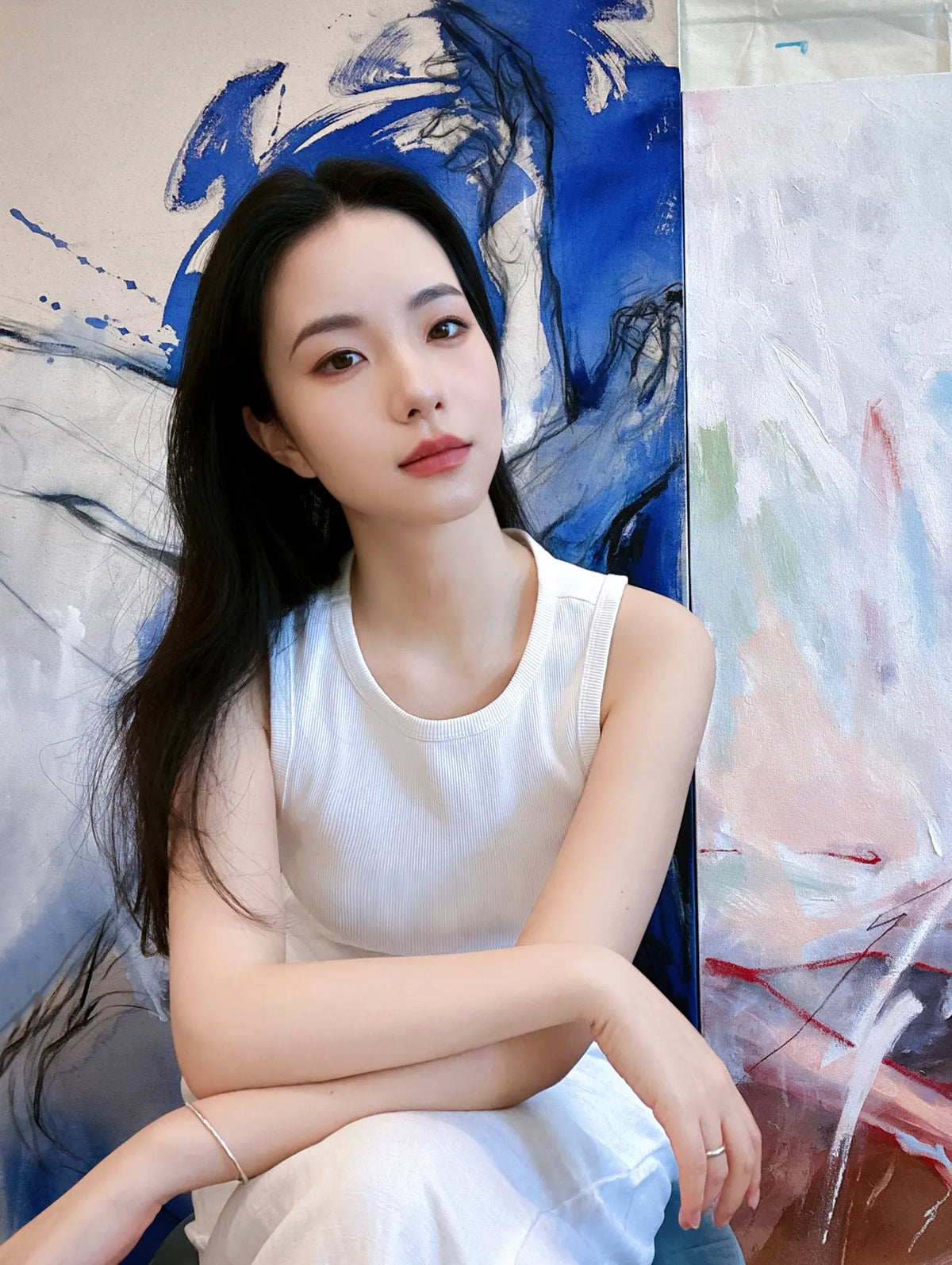 Chinese figurative artist Via Li in her studio, seated in front of large-scale blue and white figurative paintings.