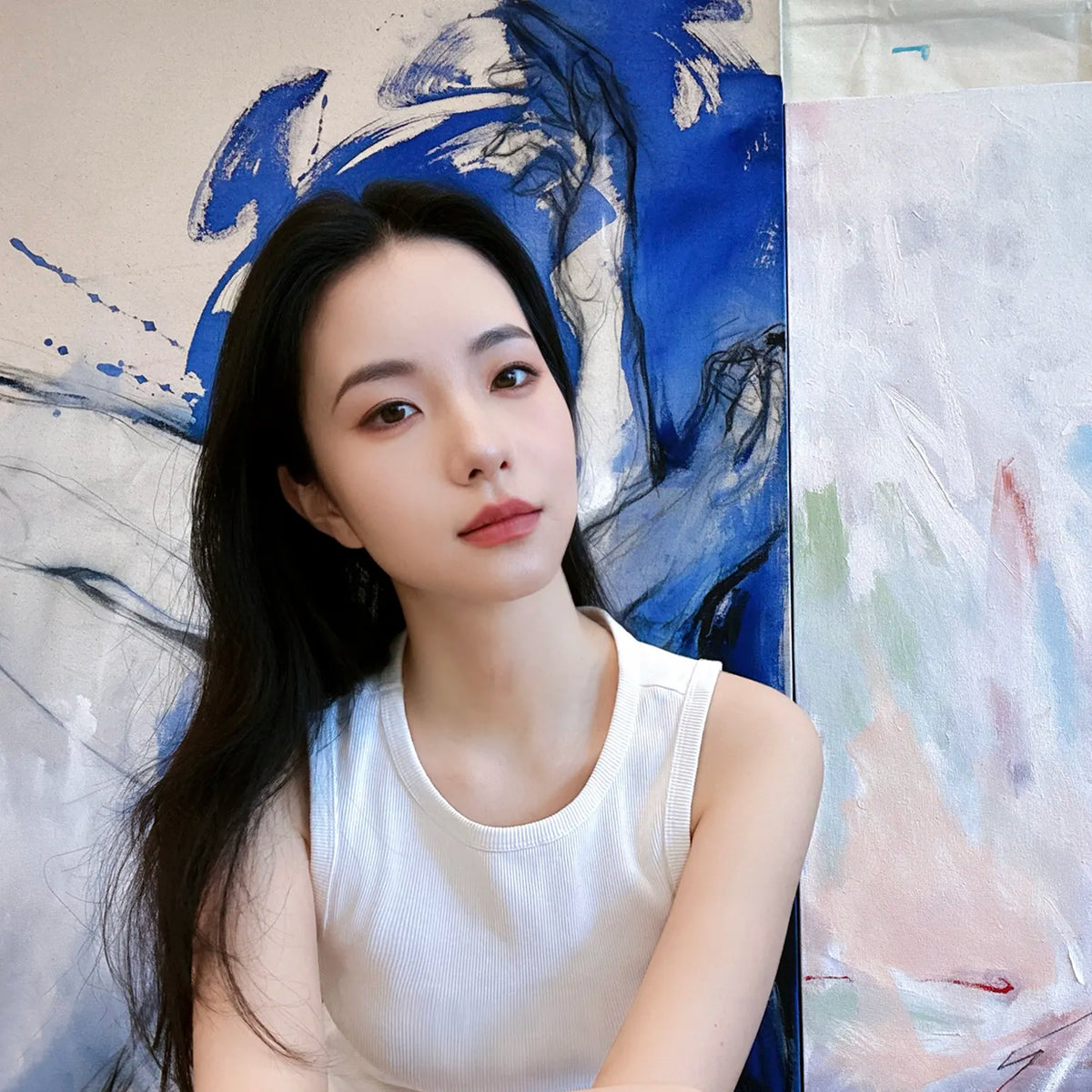 Chinese figurative artist Via Li in her studio, seated in front of large-scale blue and white figurative paintings.